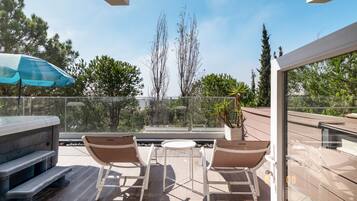 Eine Dachterrasse mit Whirlpool, zwei Liegestühlen und einem Tisch.