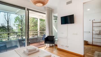 Un dormitorio moderno con un ventanal grande, un televisor de pantalla plana, una cama con toallas ordenadas y un balcón con una silla.