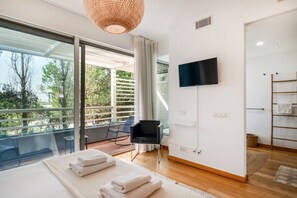 Een moderne slaapkamer met een groot raam, een flatscreen televisie, een bed met netjes gevouwen handdoeken en een balkon met een stoel.
