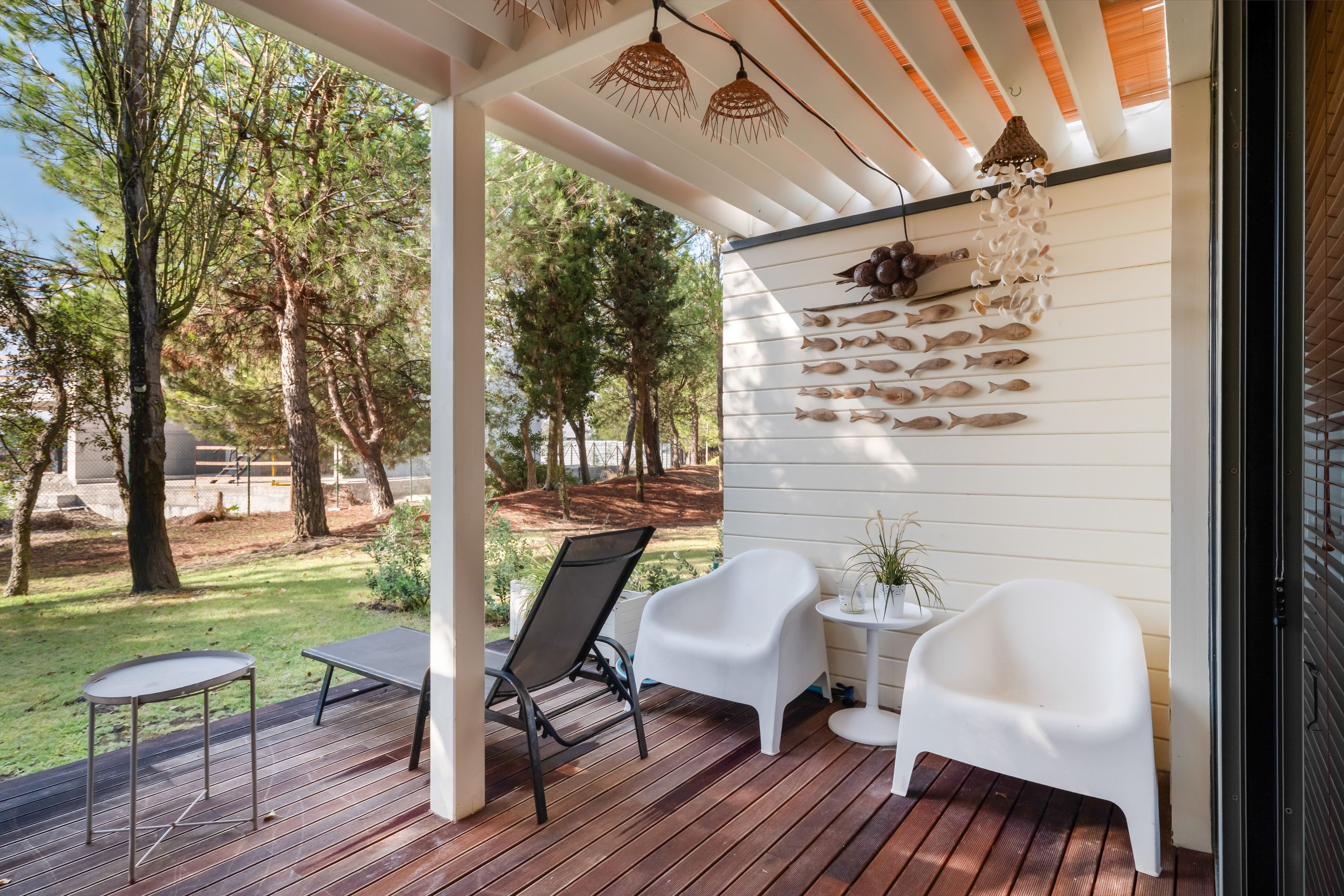 A covered outdoor seating area with two chairs and a table, surrounded by a wooden deck and a garden view.