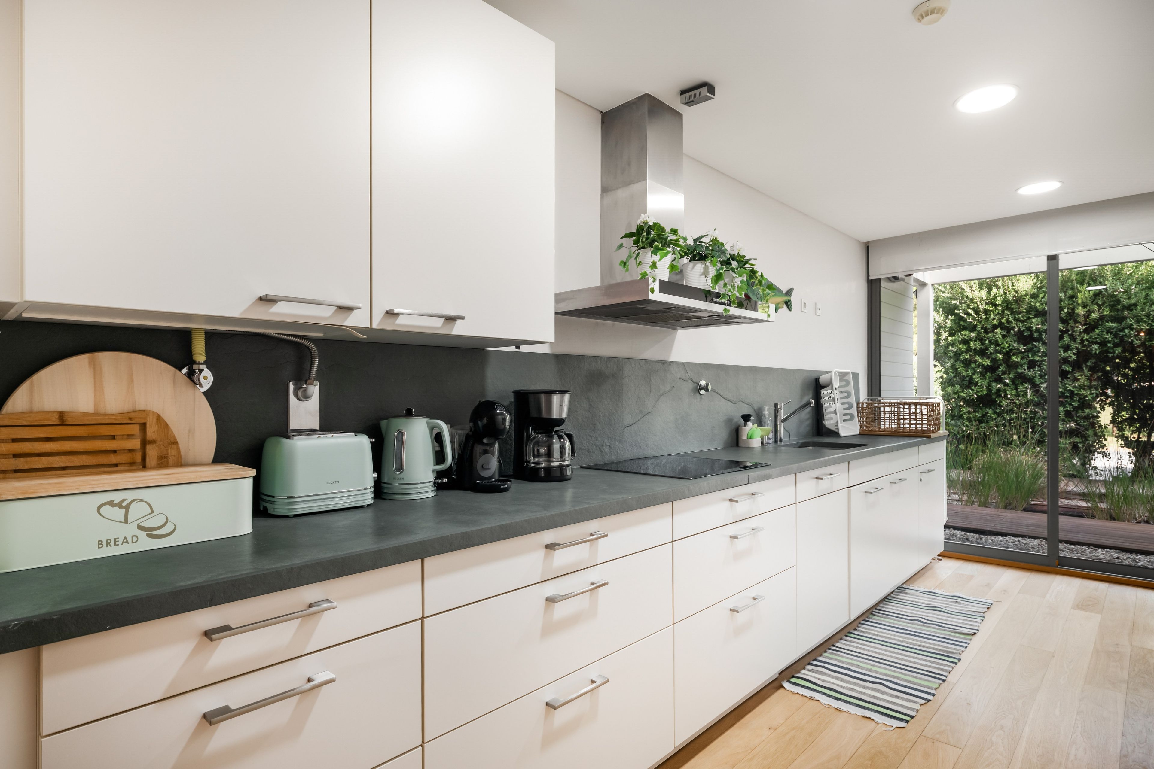 Une cuisine moderne avec des meubles blancs, un plan de travail noir et une cuisinière encastrée.