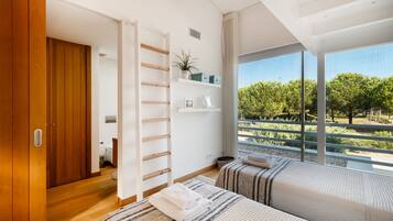 A modern bedroom with a wooden wardrobe, a built-in shelf with decorative items, a large window with a view of trees, and a bed with a striped blanket.