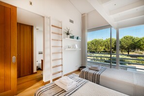 Un dormitorio moderno con un armario de madera, estante empotrado con adornos, un ventanal con vista a árboles y una cama con manta a rayas.