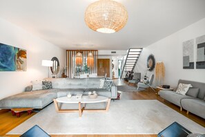 A modern living room with a grey sectional sofa, a round coffee table, and a large woven light fixture. - Holiday Home 'Tróia - Amazing Places' with Wi-Fi and Air Conditioning (Grândola)
