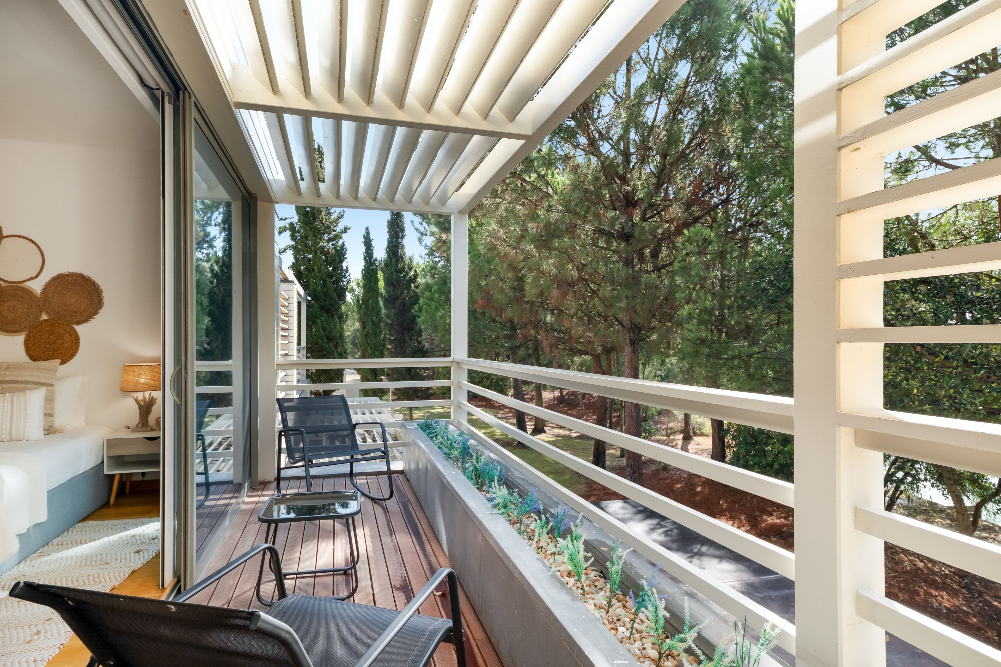 A balcony with a view of a forest, a table with chairs, and a sofa.