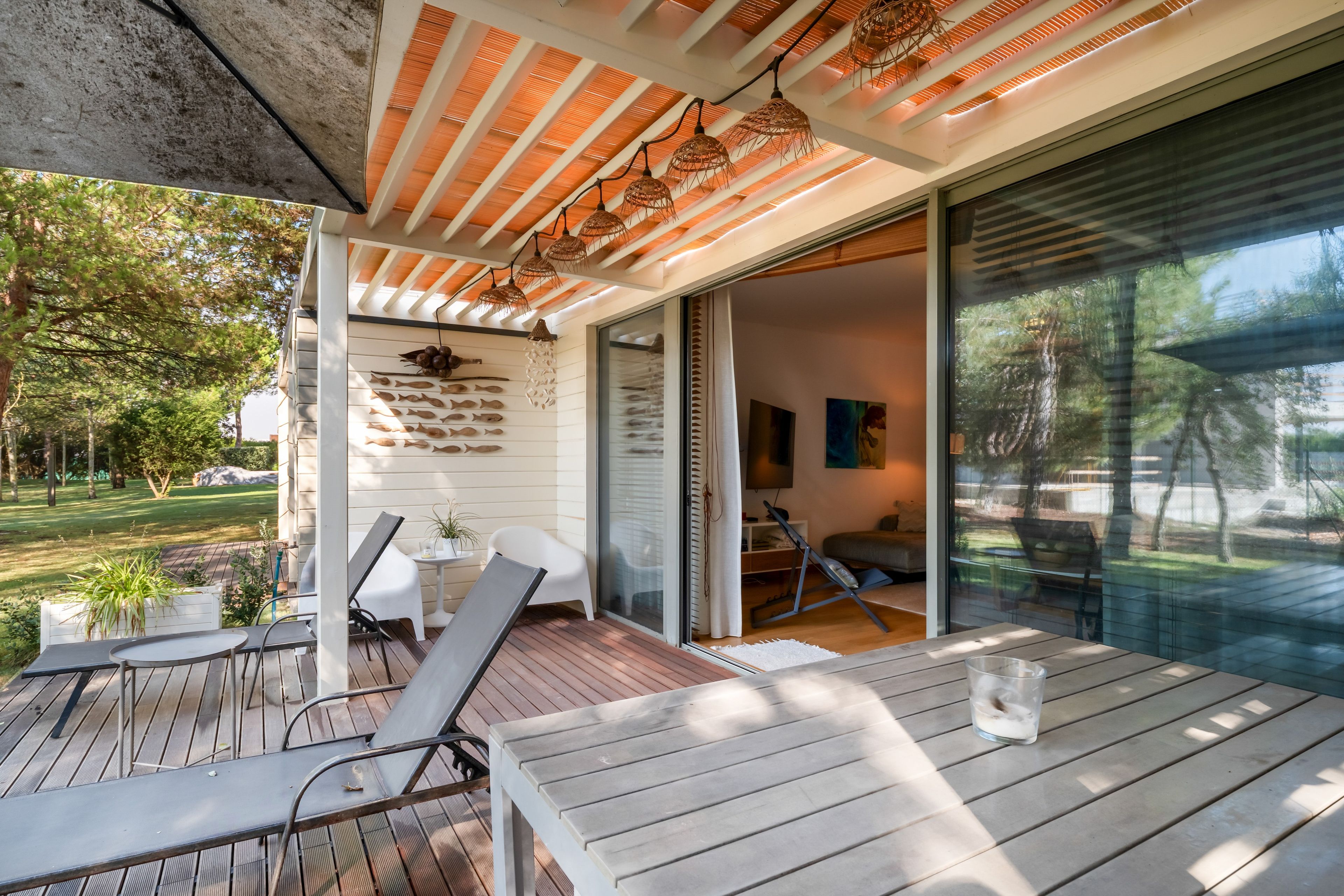 A modern outdoor patio with wooden flooring, metal chairs, and a glass door leading to an interior space.