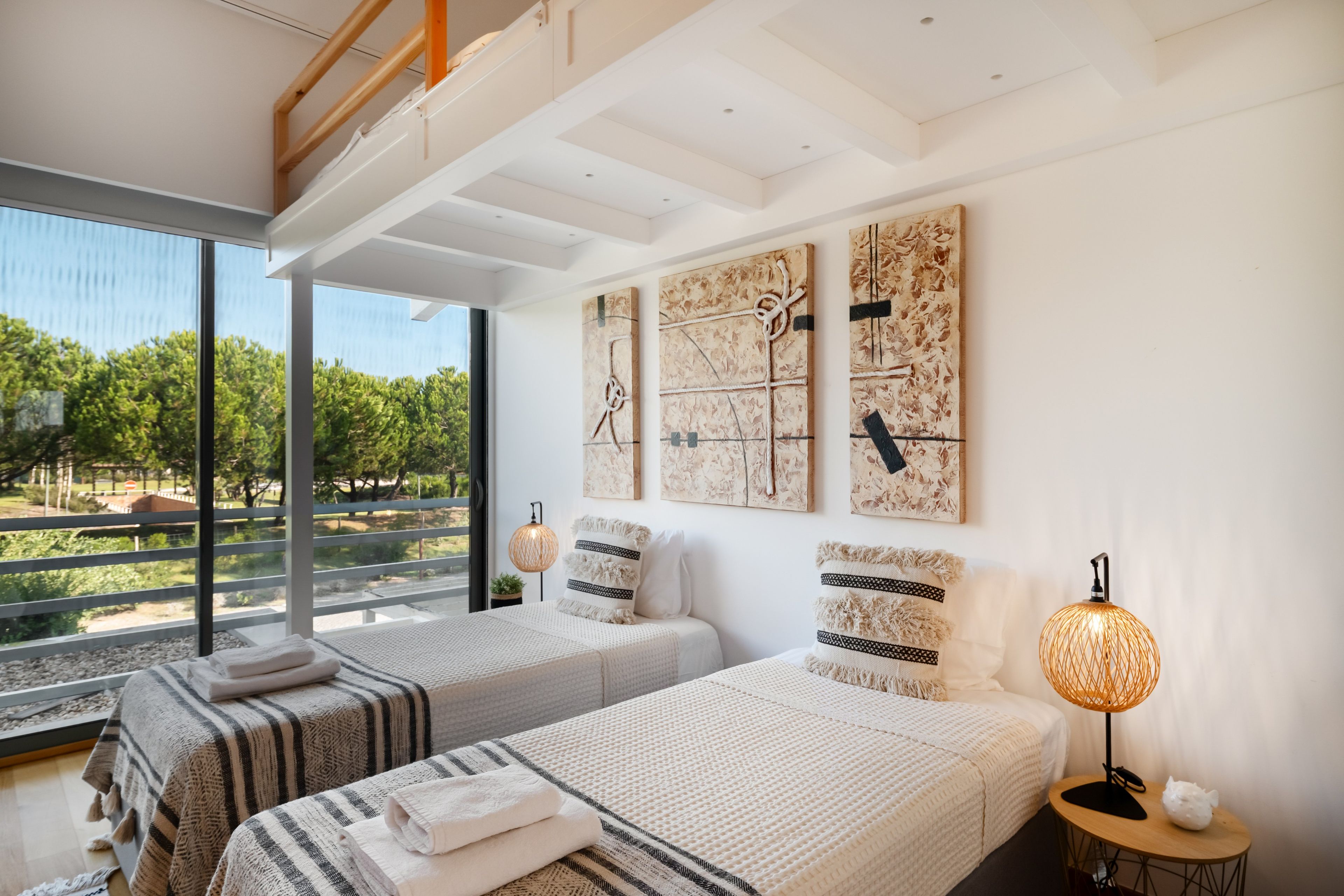 Un dormitorio moderno con dos camas, ventanas amplias y obras de arte en las paredes.