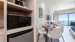A modern kitchen with a built-in microwave and dishwasher, a dining area with white chairs, and a large window overlooking the sea. - One 1702A Hotel Room:🌌 Star Wars Oceanfront Hotel Room| Sonoran Star Resort ⭐🌊 (Puerto Peñasco)