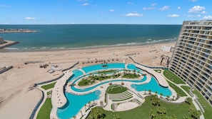 Et resort med en stor swimmingpool, direkte til stranden og en høj bygning.