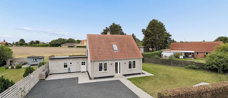 A two-story house with a red-tiled roof, a fenced yard, and a gravel driveway.