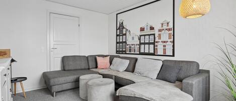 A modern living room with a grey sectional sofa, ottomans, a white door, and a framed cityscape artwork.