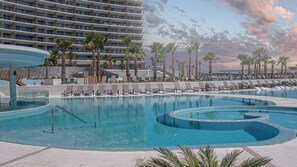 Ein Hotelpool mit Liegestühlen und Palmen, umgeben von einem Hochhaus.