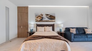 Ein Schlafzimmer mit einem Bett, einem blauen Schlafsofa, einem Holzschrank und einem Bild von Booten an der Wand.