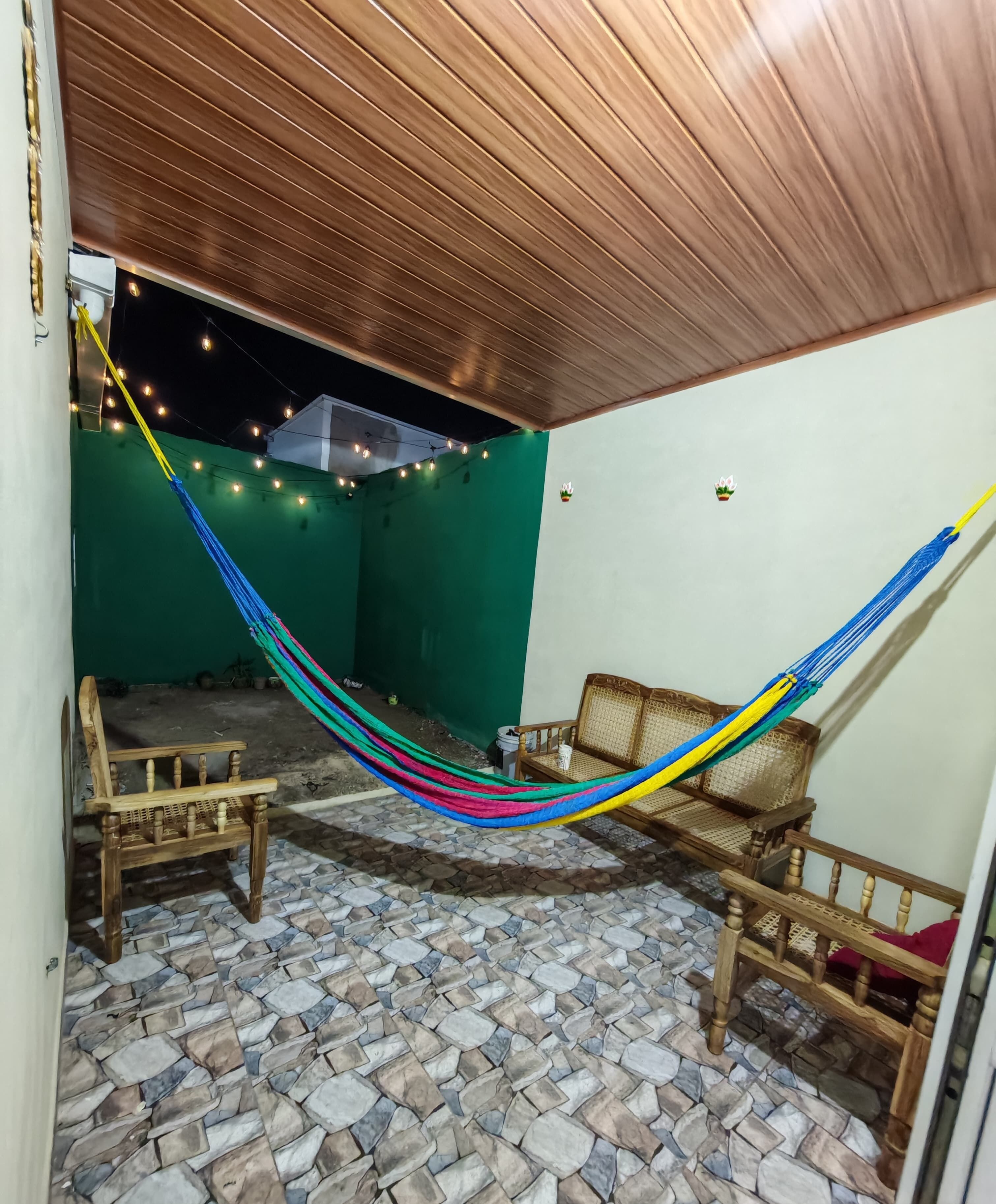 A hammock between wooden furniture in a room with a tiled floor and a green wall.