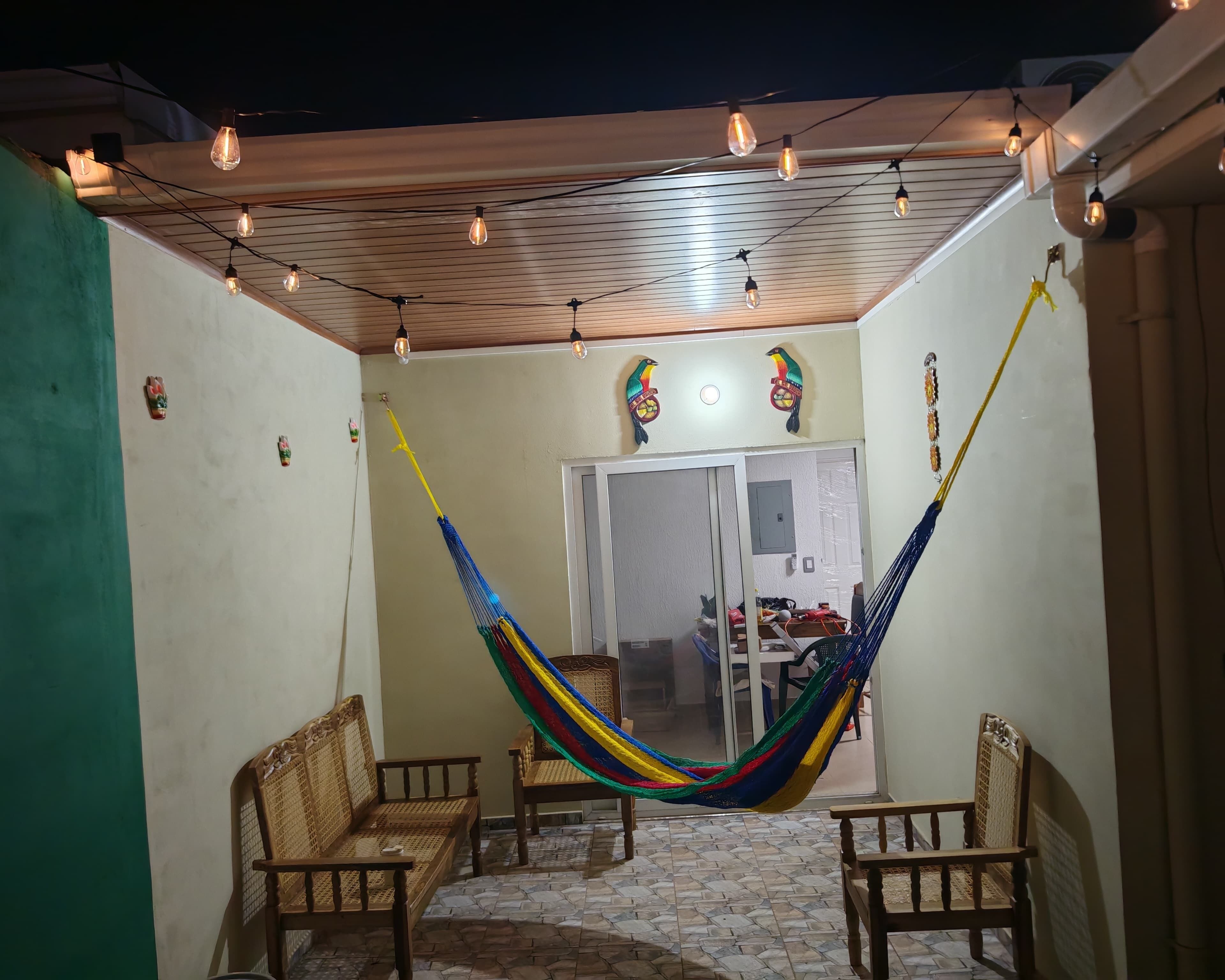 A patio with a hammock, wooden chairs, and string lights.