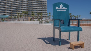 A beach chair and a wooden bench on a sandy beach with a hotel in the background. - One 1501 : The Sunset Suite (Puerto Peñasco)