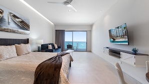 Ein modernes Hotelzimmer mit einem großen Bett, einem Fernseher, einem Balkon mit Blick auf den Pool und einem Deckenventilator.