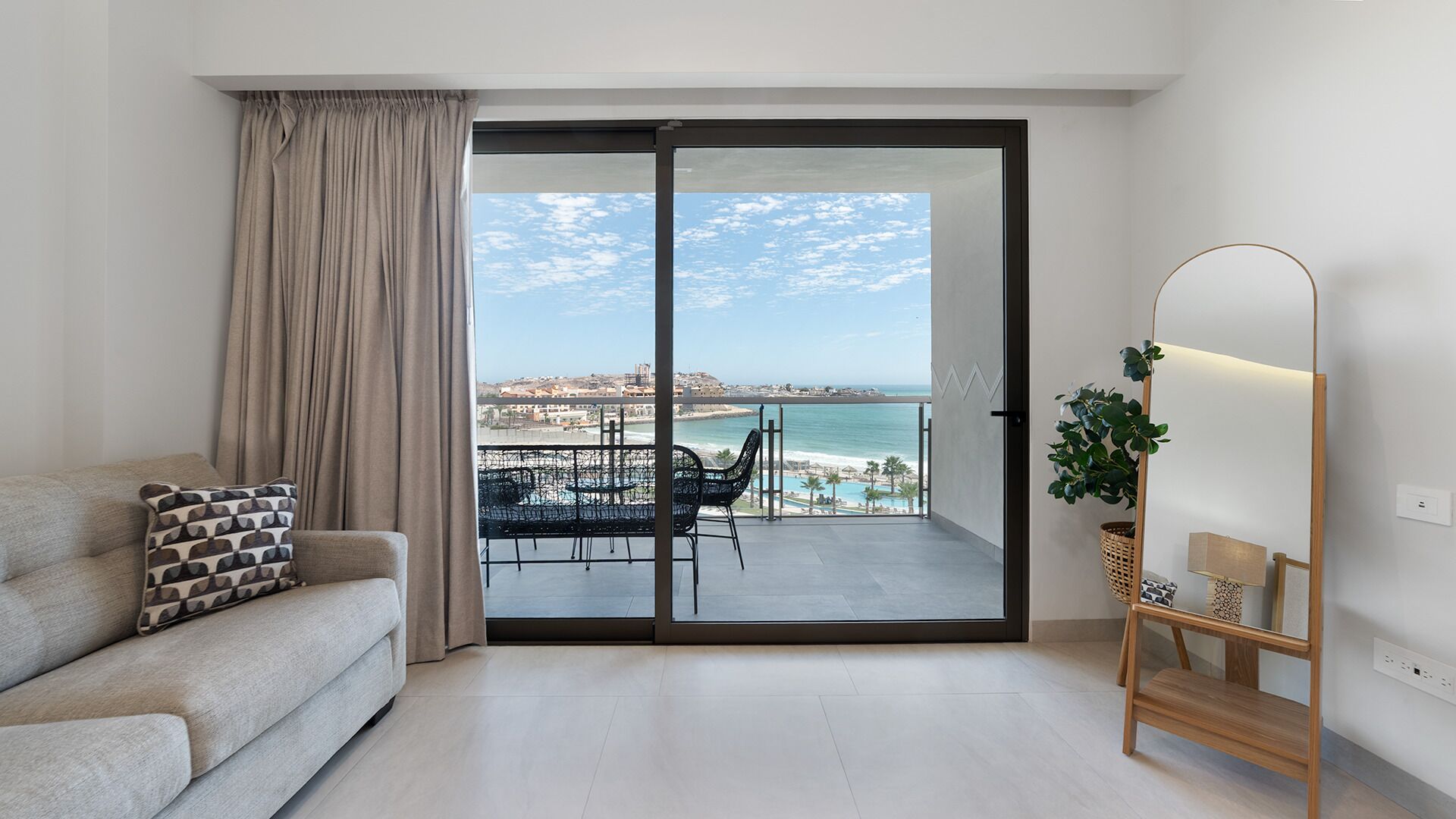 A modern living room with a sofa, a view of the sea, and a balcony with outdoor furniture.