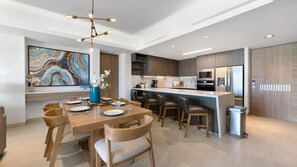 A modern kitchen with a central island, bar seating, and a dining area with a large painting. - Two 501Full: The Ultimate Beachfront Getaway (Puerto Peñasco)