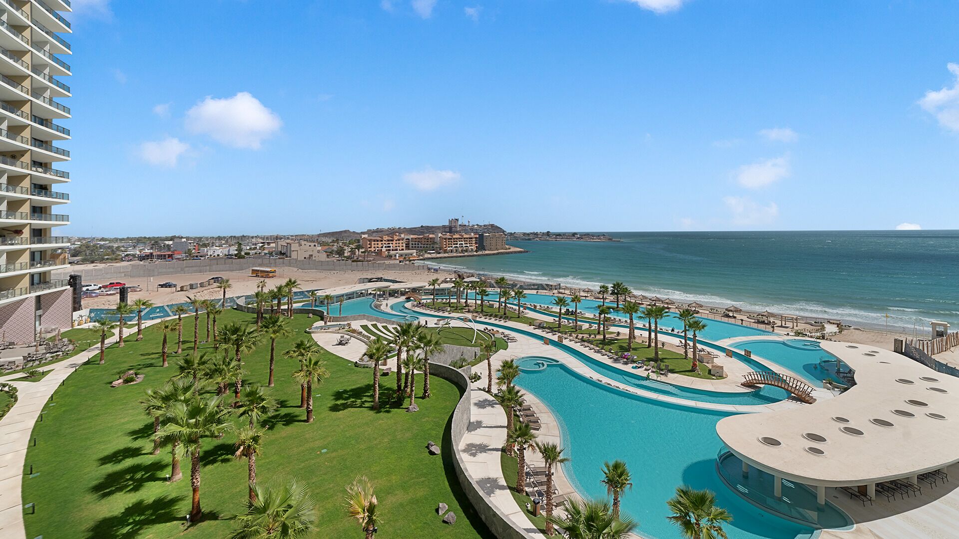 Ein Resort mit großem Poolbereich, Palmen und Blick auf Strand und Meer.