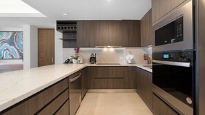 A modern kitchen with wooden cabinets, a marble countertop, a built-in oven, and a coffee maker. - Two 501Full: The Ultimate Beachfront Getaway (Puerto Peñasco)