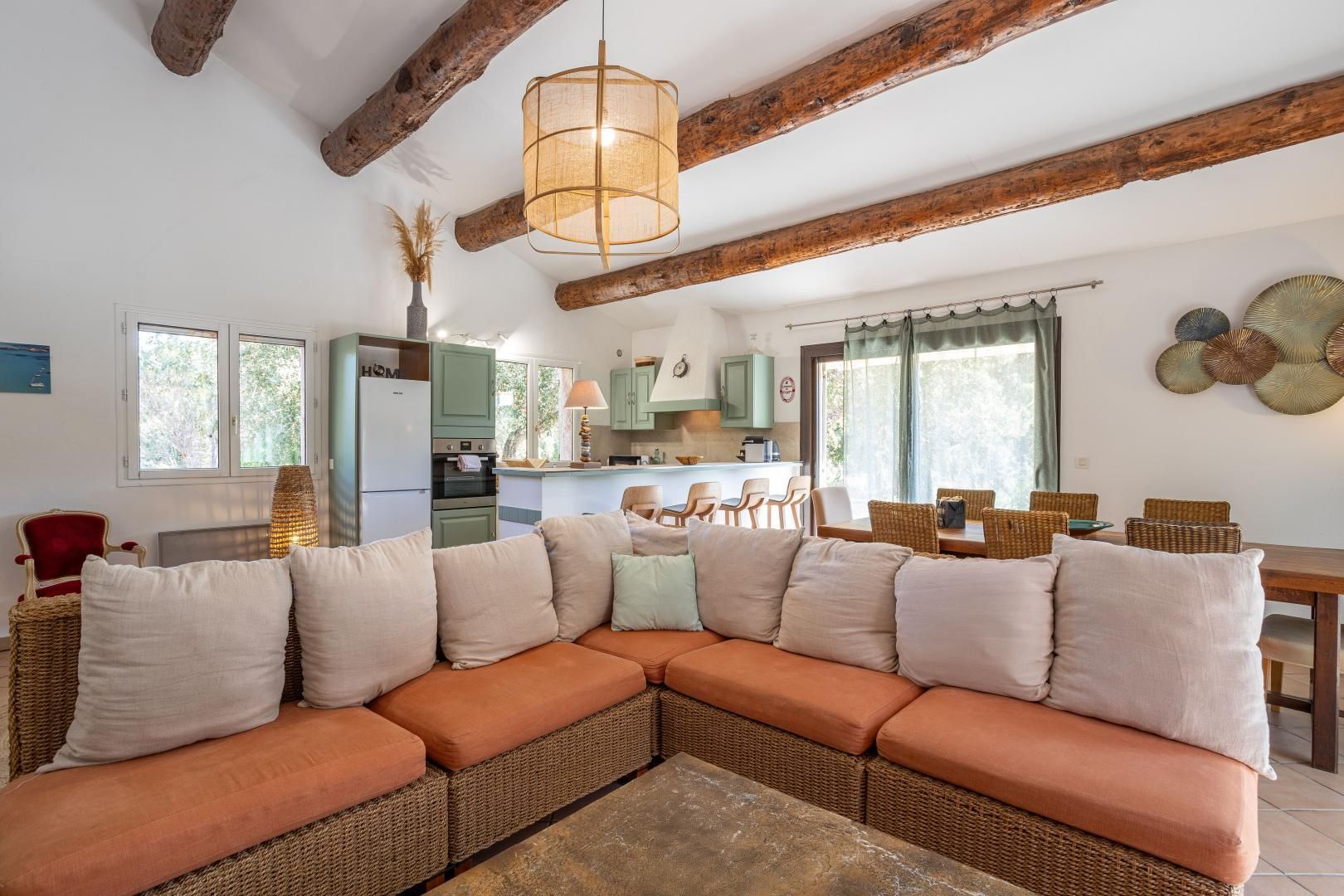 Una sala acogedora con un sofá modular, un comedor y una cocina con vigas de madera.