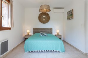 A bedroom with a bed, two bedside lamps, a wall-mounted air conditioner, a window with curtains, and a wall art piece. - Villa Gioia - SAN GAVINO DI CARBINI (SAN GAVINO DI CARBINI)