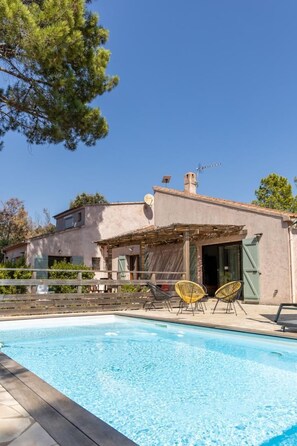 Une maison avec une piscine, un espace salon extérieur et une pergola.