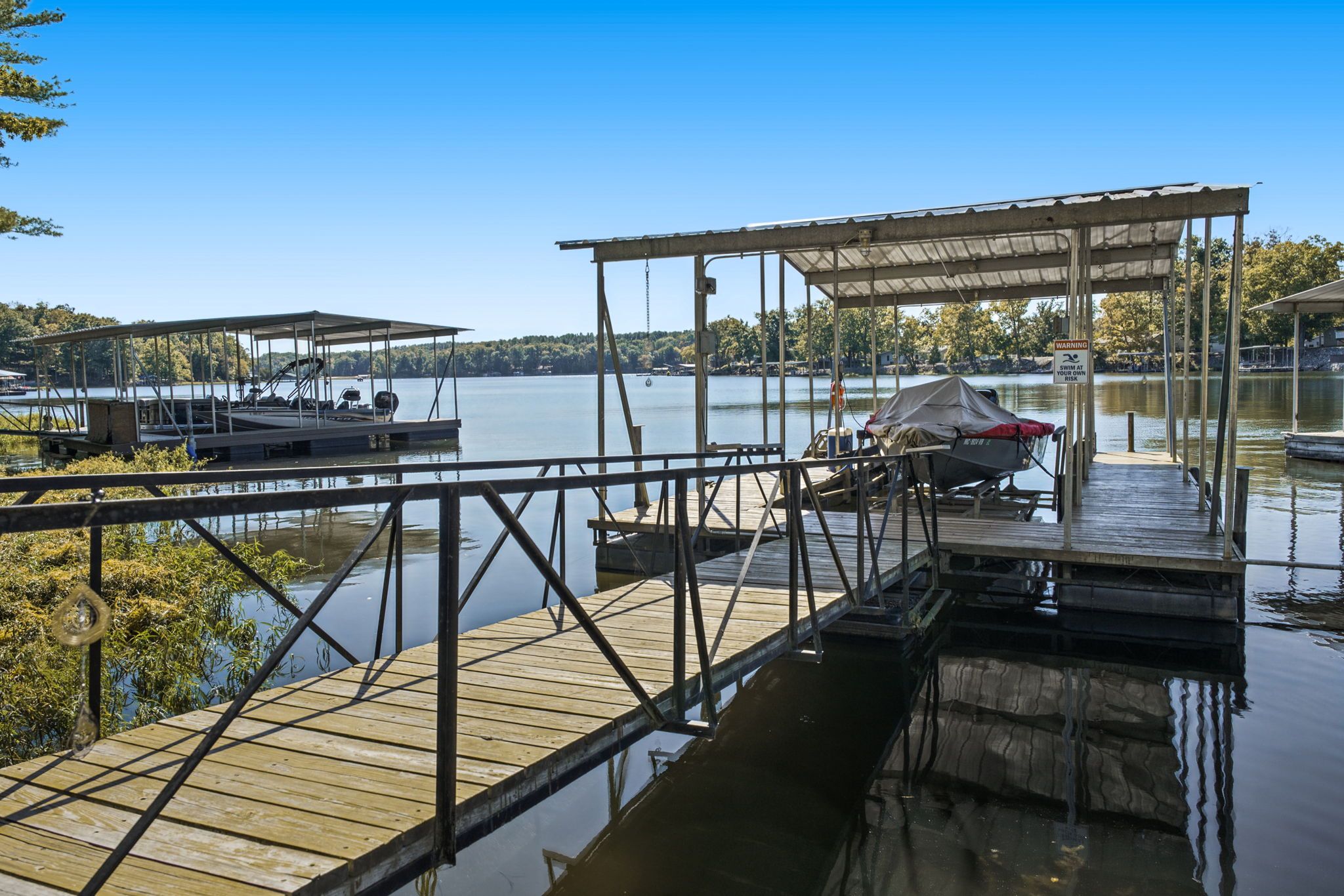 A wooden dock extending into a calm lake with a covered seating area and a boat docked nearby.