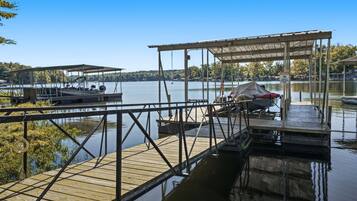 A wooden dock extending into a calm lake with a covered seating area and a boat docked nearby.