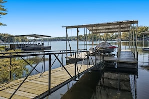 A wooden dock extending into a calm lake with a covered seating area and a boat docked nearby.