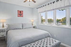 A bedroom with a bed, nightstands, a window with a view, and a ceiling fan.