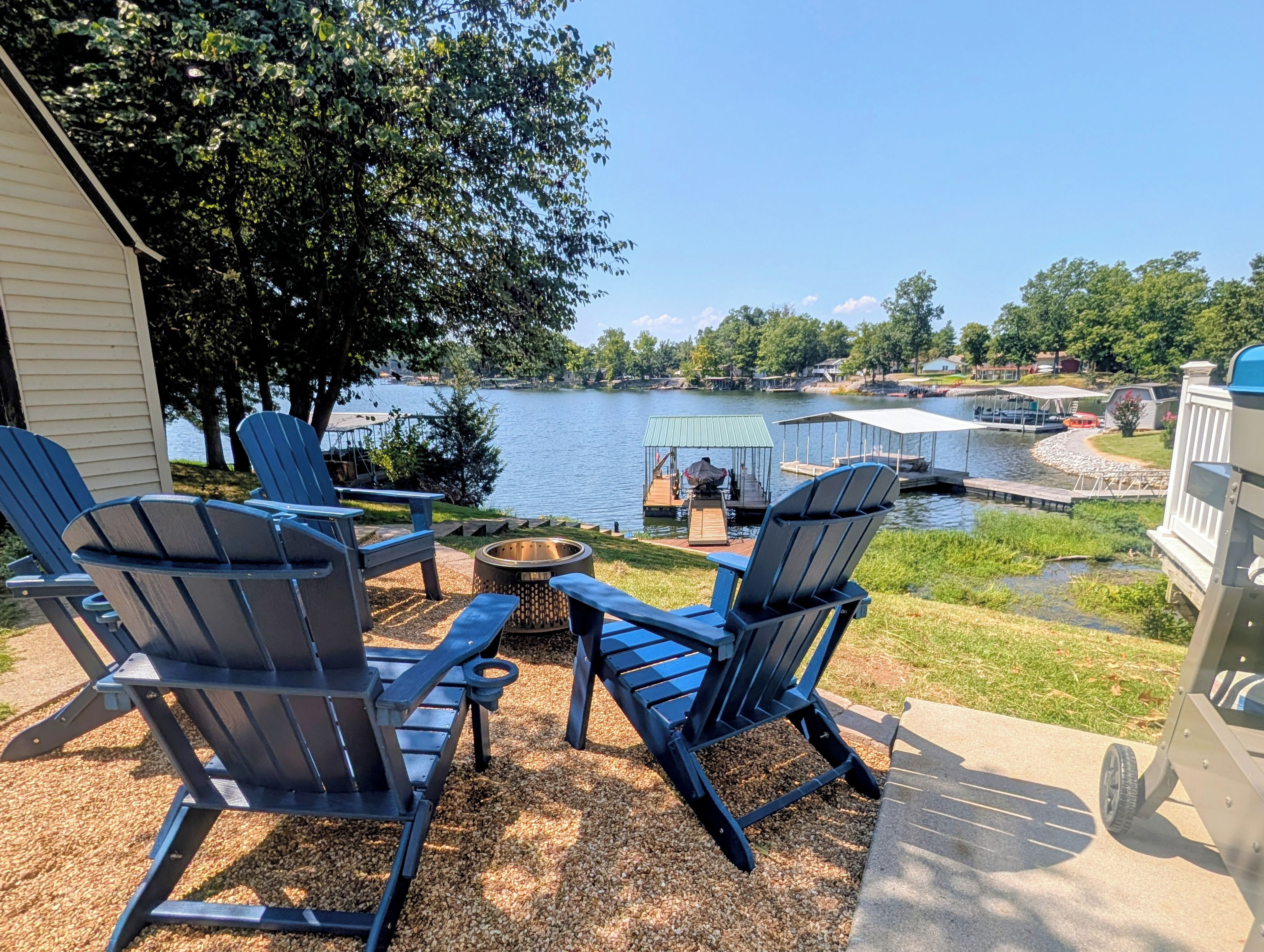 Une terrasse au bord du lac, avec des fauteuils Adirondack, un foyer et une vue sur un quai et un bateau.