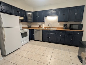 A kitchen with dark cabinets, a white refrigerator, a stove, a dishwasher, a sink, and a microwave.
