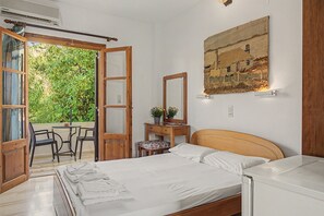 Ein Schlafzimmer mit Bett, Nachttisch, Stuhl, Schreibtisch und einem großen Fenster mit Blick ins Grüne.