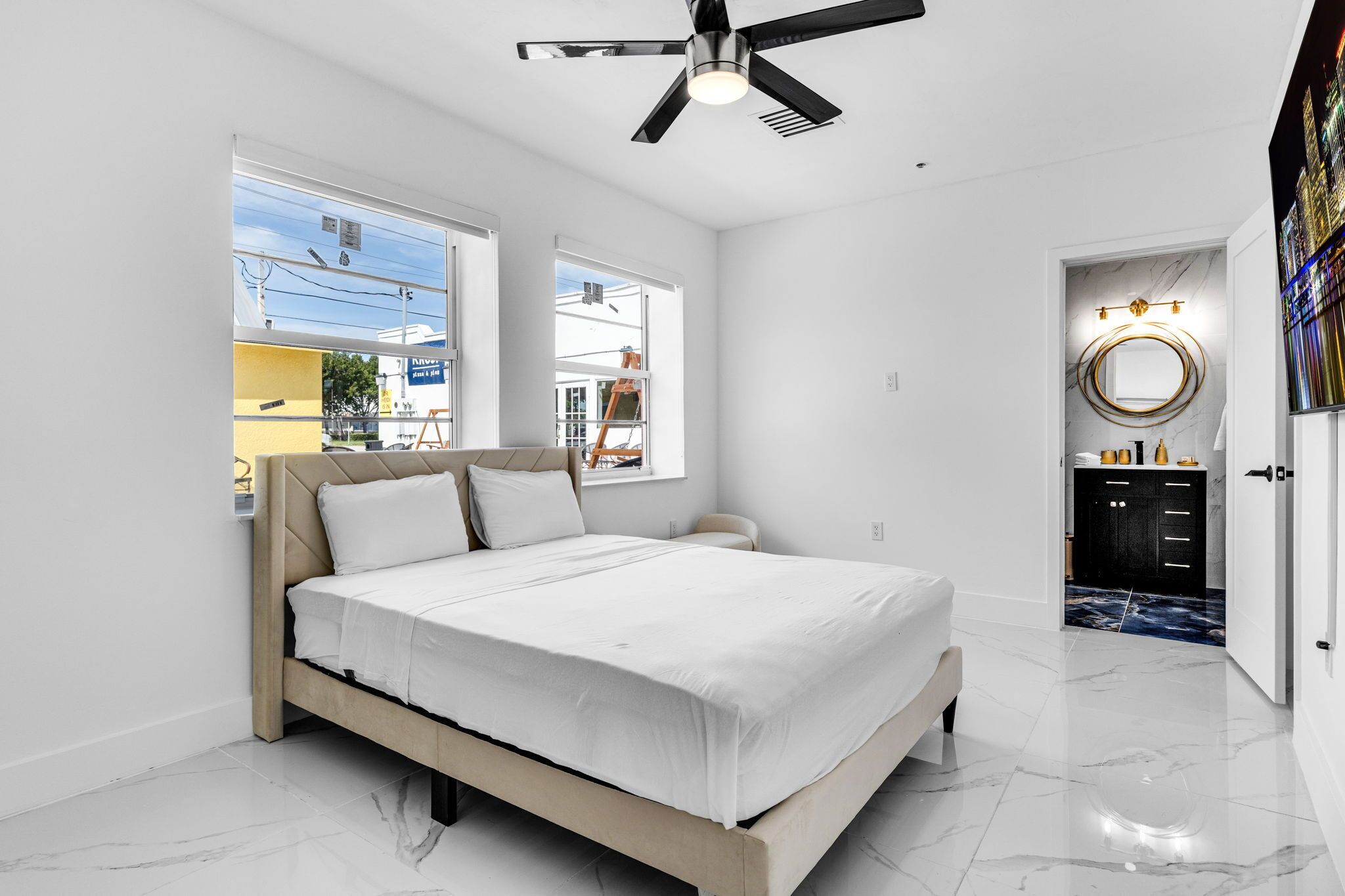 A modern bedroom with a bed, a ceiling fan, and a view of the outside.