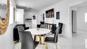Uma sala de jantar moderna com uma mesa redonda, cadeiras pretas e uma parede branca com uma pintura de paisagem urbana.