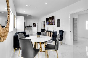 Een moderne eetruimte met een ronde tafel, zwarte stoelen en een witte muur met een stadsgezicht schilderij.