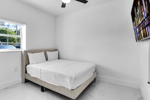 Quarto com cama, janela e ventoinha no teto.