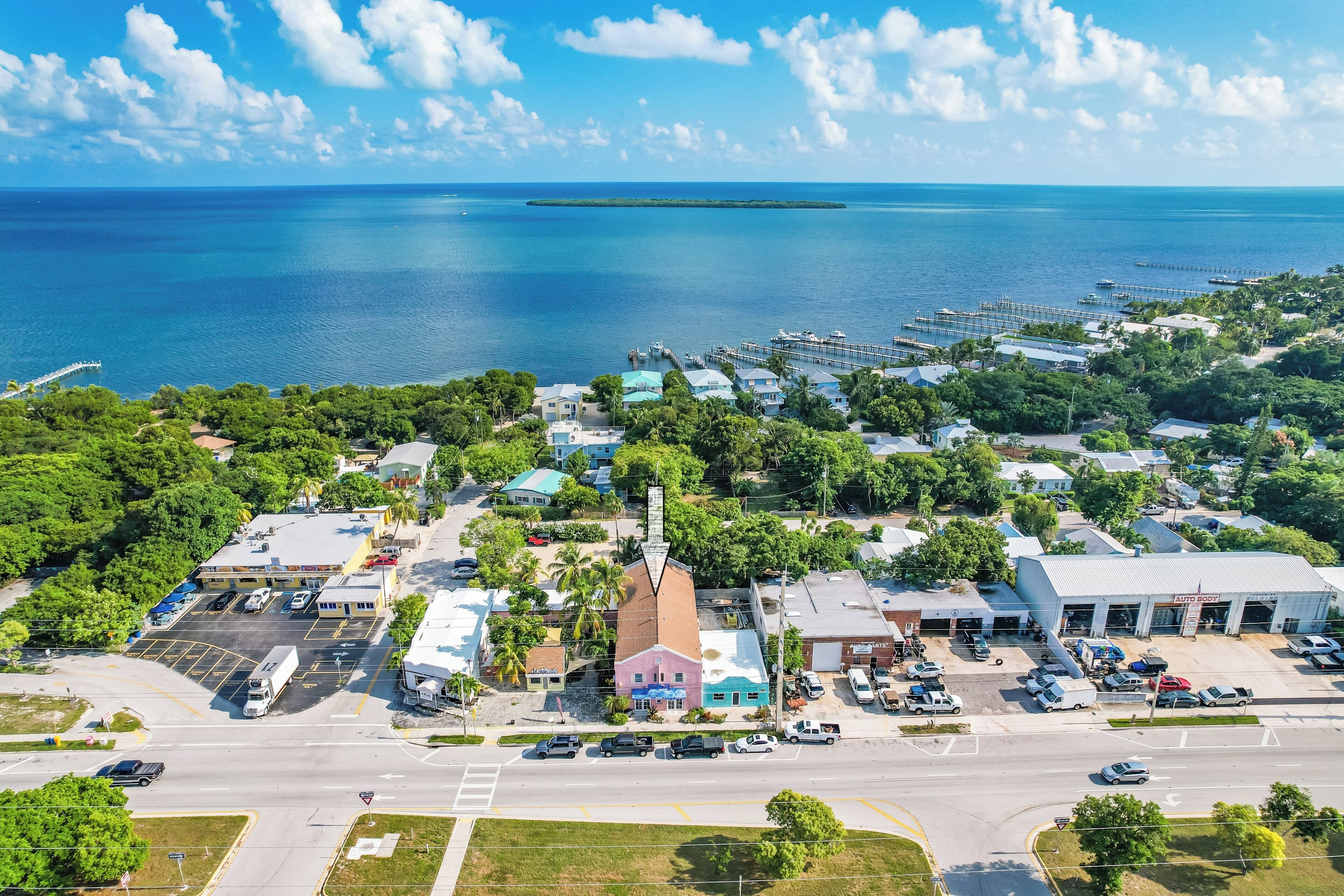 An aerial view of a coastal town with a marina, a prominent building with a red roof, and a clear view of the ocean.