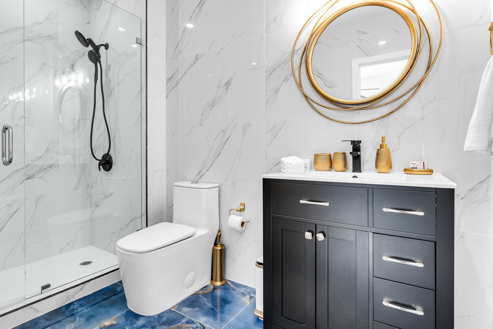 A modern bathroom with a glass-enclosed shower, a white toilet, a black vanity with gold accents, and a gold-framed mirror.