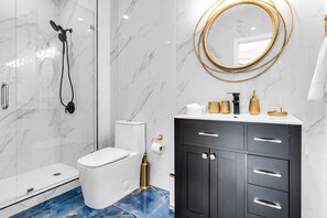 Een moderne badkamer met een douchecabine van glas, een wit toilet, een zwart wastafelmeubel met gouden accenten en een spiegel met gouden lijst.