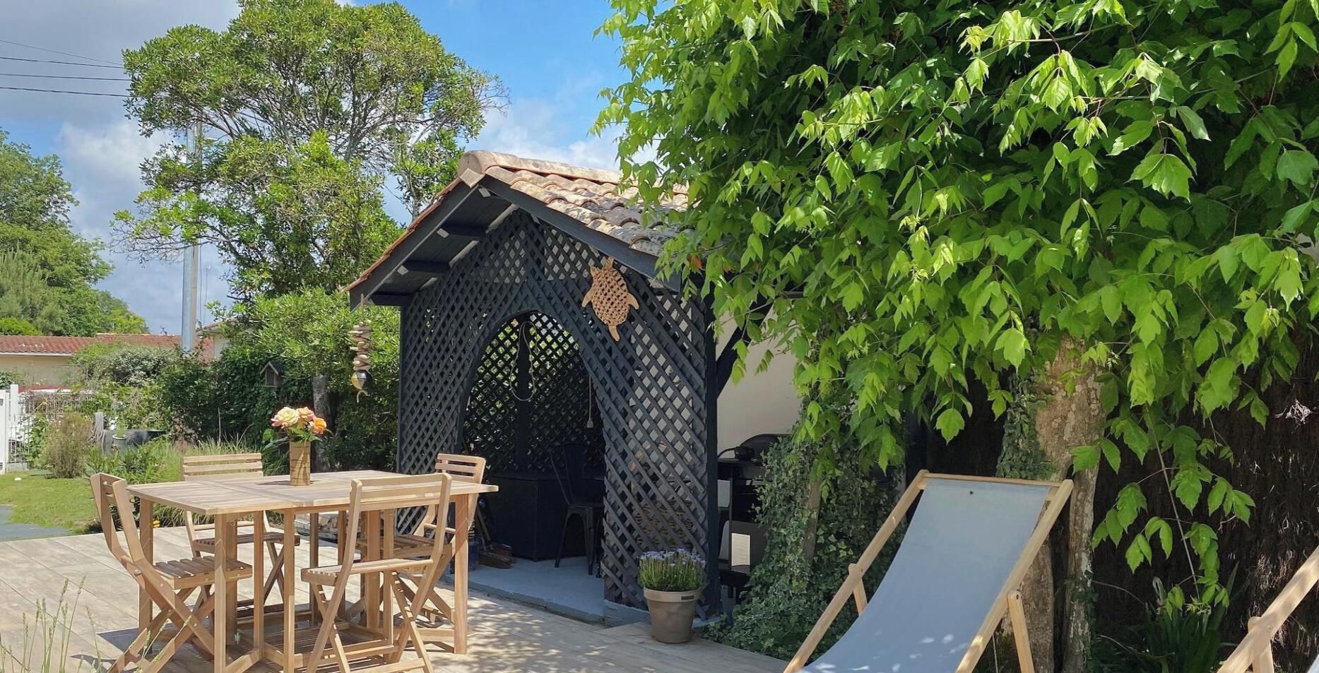 A wooden outdoor seating area with a table and chairs, a small garden, and a decorative wooden structure.