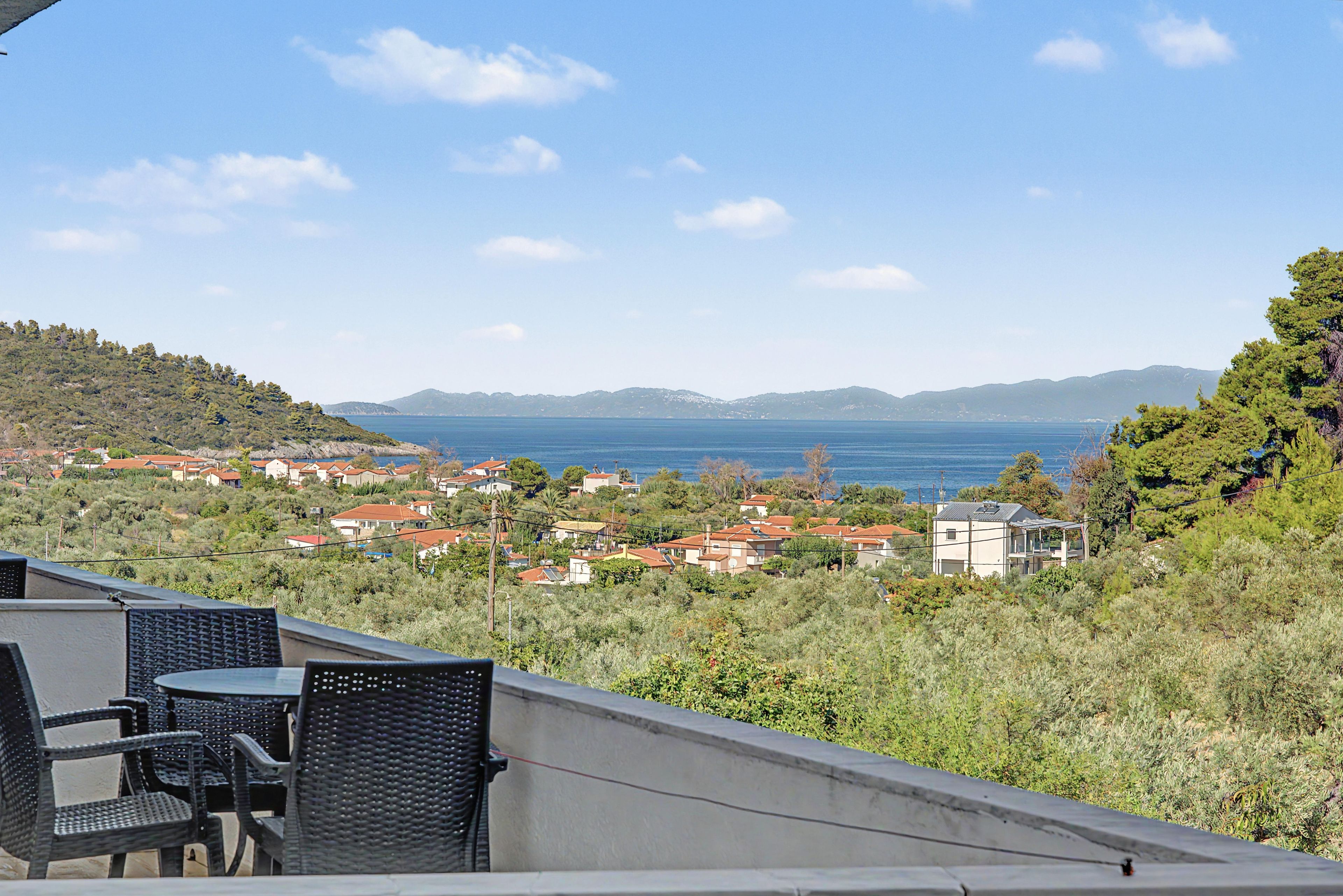 A terrace with outdoor furniture overlooking a coastal town and the sea.
