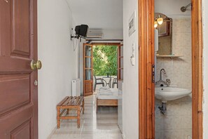 Ein schmaler Flur führt zu einem Badezimmer mit einem Waschbecken und einem Fenster mit Blick auf Grünflächen.