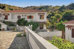 A traditional white building with a tiled roof, a stone-paved courtyard, and a view of a hillside. - Room 'Orama 31' with Sea View, Wi-Fi and Air Conditioning (Εύβοια)
