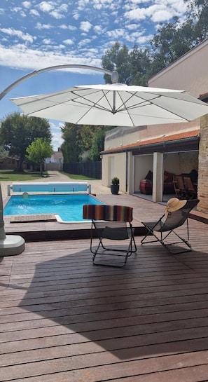 A swimming pool with a wooden deck, two lounge chairs, and a large umbrella. - Vrbo Property (LESPARRE MEDOC)