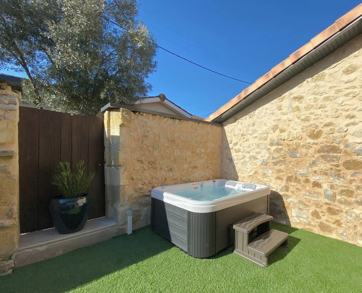Un jacuzzi en un patio trasero con paredes de piedra, césped artificial y una planta en maceta.