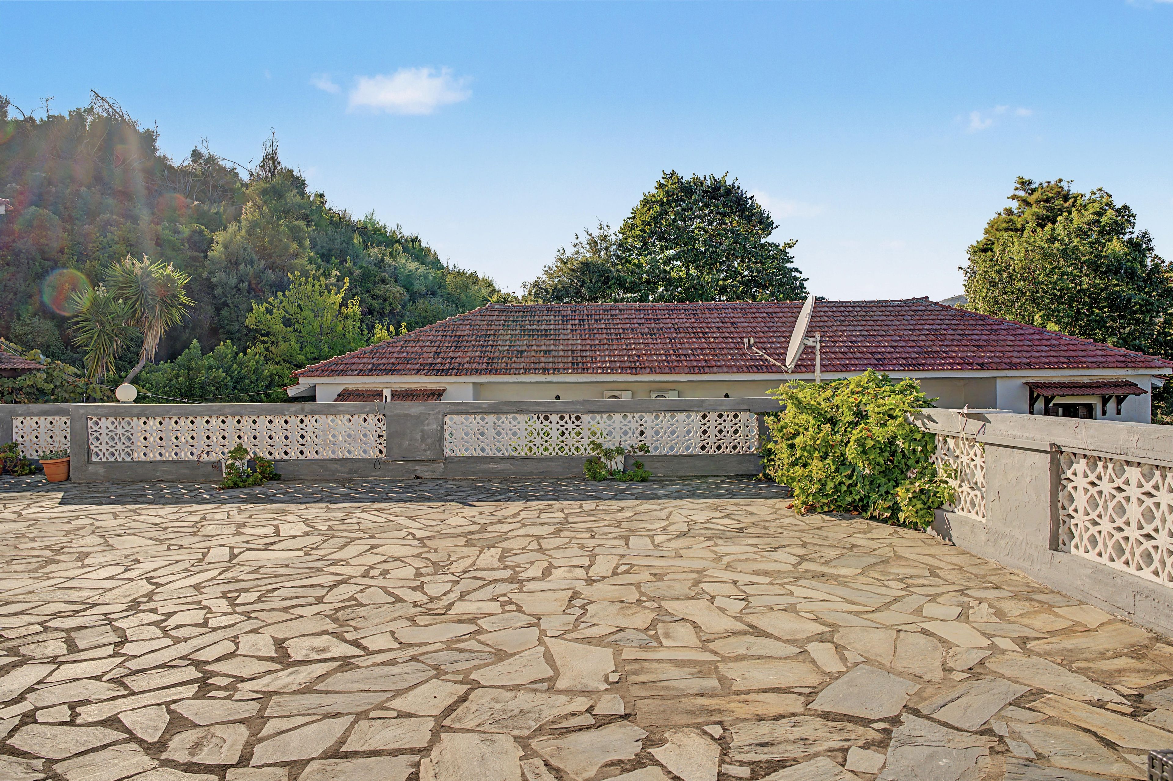 A building with a tiled roof, stone flooring, and a white fence with lattice panels.