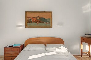 Ein Schlafzimmer mit einem hölzernen Bett, einem Nachttisch, einer Kommode und einem an der Wand hängenden Gemälde.